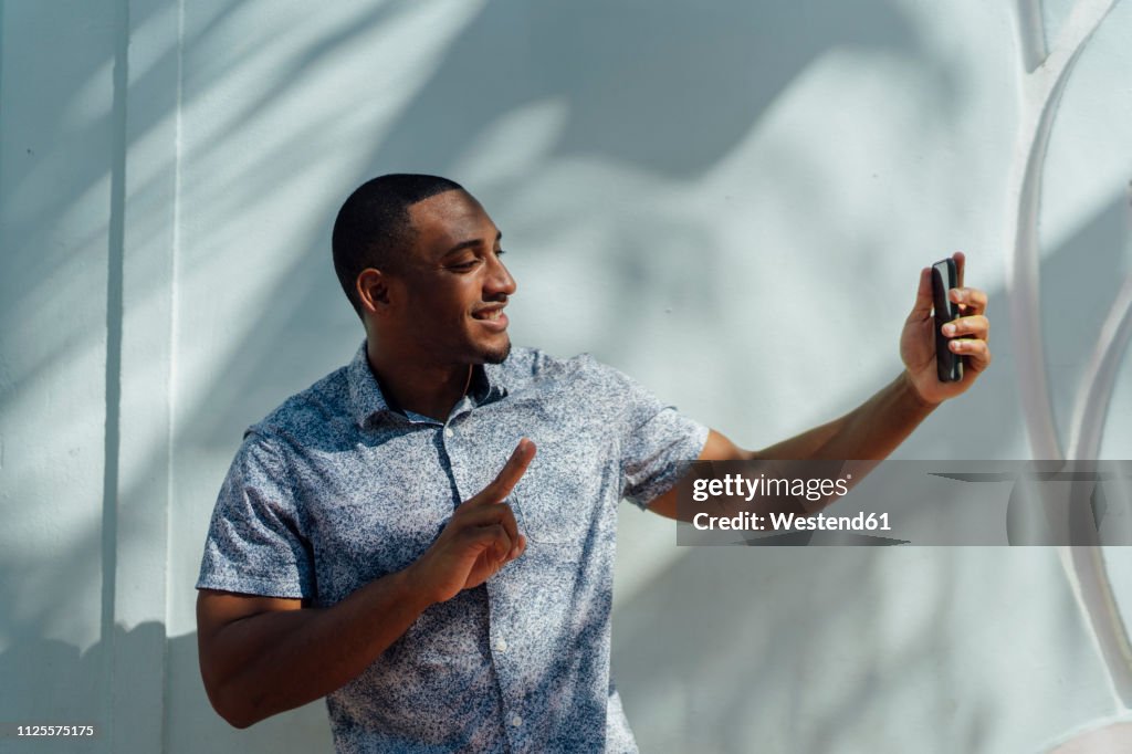 Smiling young man wearing shirt taking a selfie at a wall