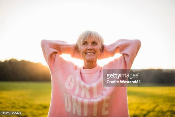 portrait of confident senior woman standing on rural meadow at sunset - frauenpower stock-fotos und bilder