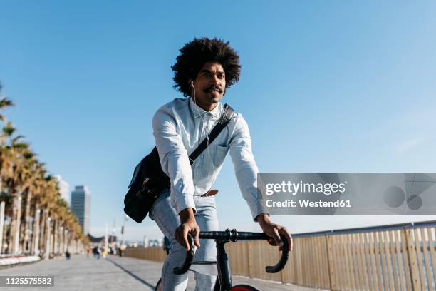 mid adult man riding bicykle on a beach promenade, listening music - elektro fahrrad stock-fotos und bilder