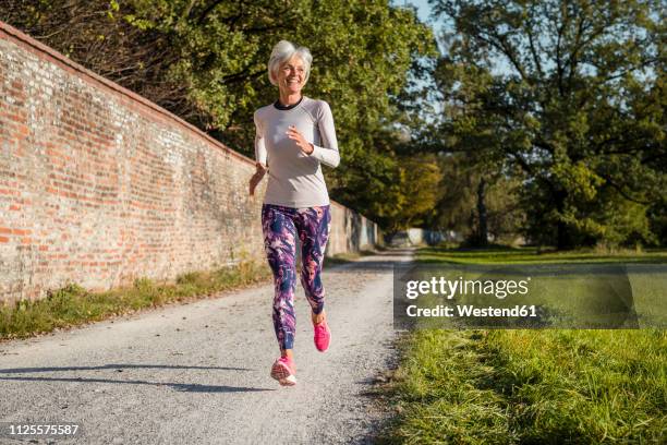 senior woman running along brick wall in a park - old woman running stock pictures, royalty-free photos & images