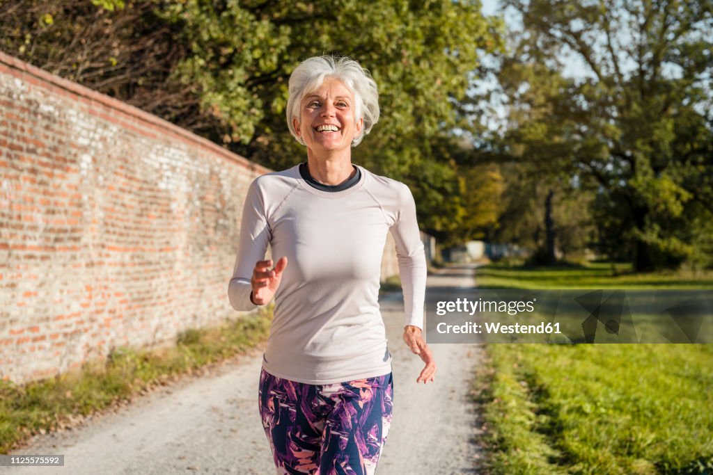 Happy senior woman running along brick wall in a park