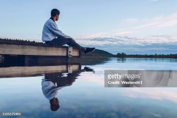 young man sitting at lake inari, looking at view, finland - inari finland bildbanksfoton och bilder