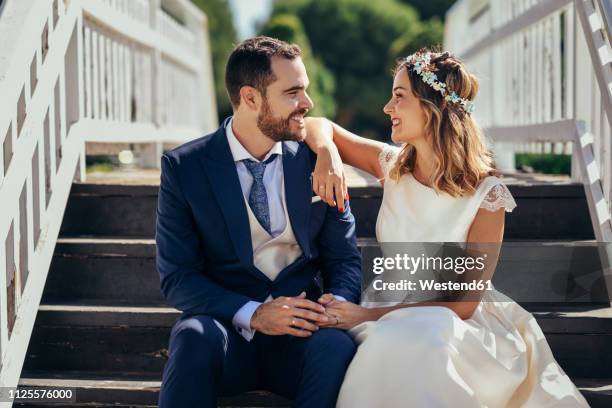 happy bridal couple sitting on stairs holding hands - married imagens e fotografias de stock