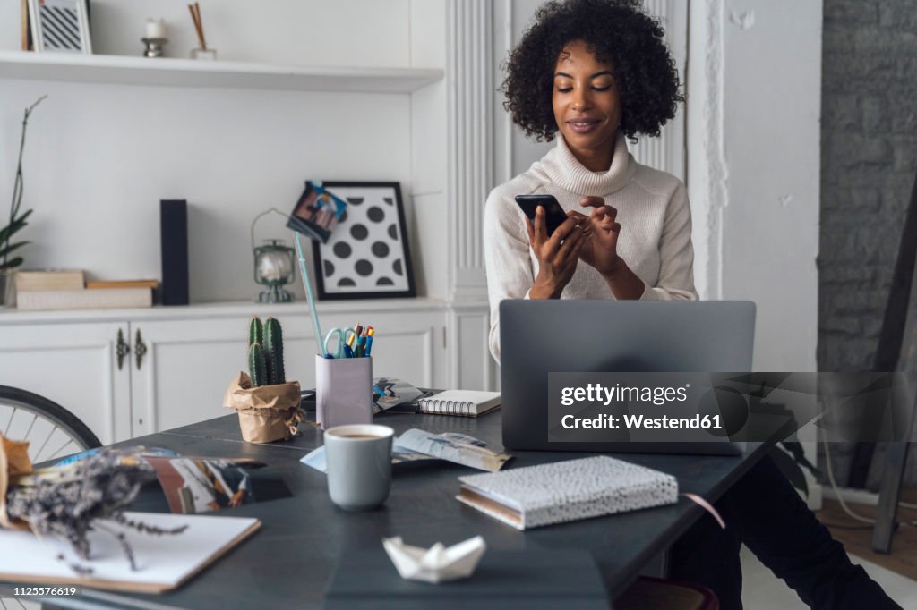 Mid adult woman working in her home office, using smartphone