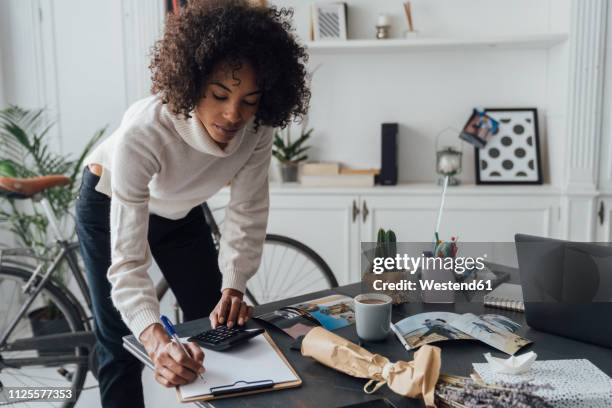 freelancer standing at hert desk, using calculater, taking notes - calculating money stock pictures, royalty-free photos & images