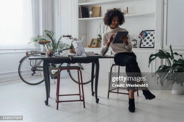 mid adult freelancer sitting at her desk, working with laptop and digital tablet - beautiful laptop on desk stock pictures, royalty-free photos & images