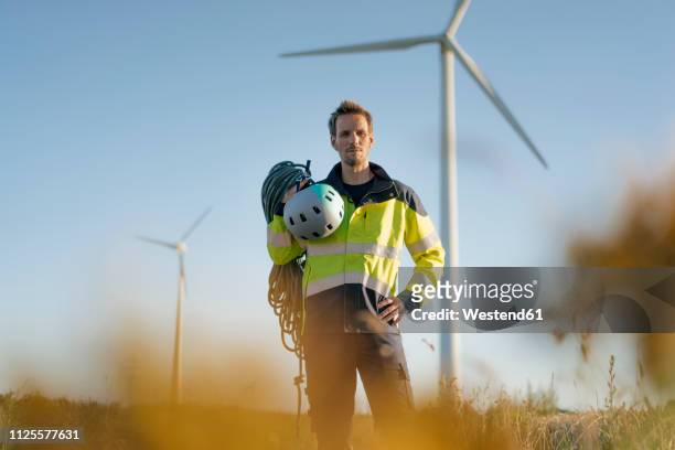 Technician standing in a field at a wind farm with climbing equipment