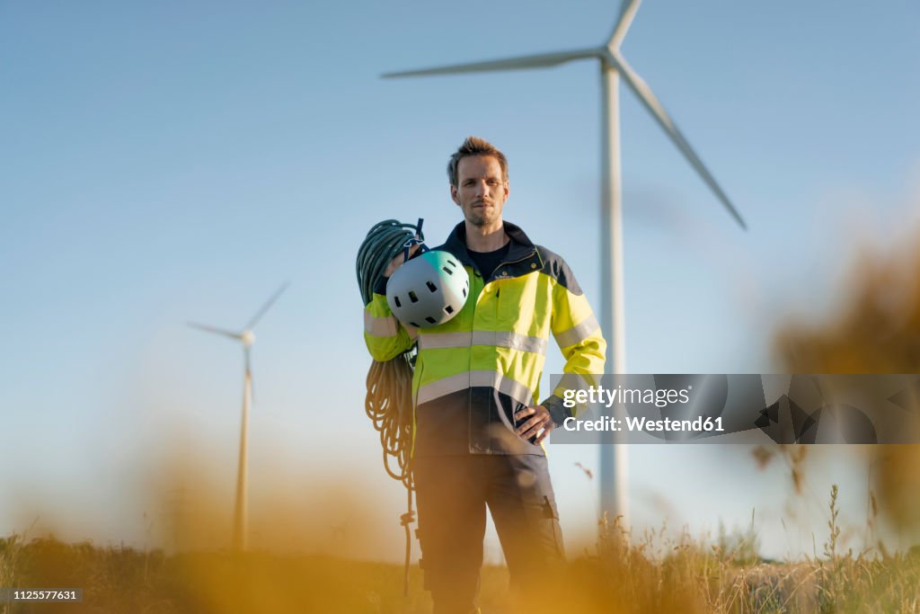 Technician standing in a field at a wind farm with climbing equipment