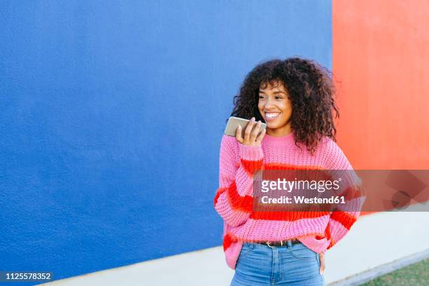 portrait of smiling young woman sending a voice message with mobile phone - lady talking on the phone stock-fotos und bilder