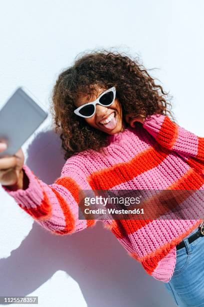 portrait of young woman wearing sunglasses taking selfie with mobile phone - taking selfie white background stockfoto's en -beelden