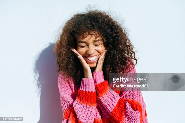 portrait of laughing young woman with curly hair against white wall - maglione foto e immagini stock