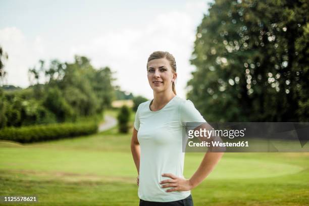 portrait of smiling sportive young woman standing in a park - sportlerin stock-fotos und bilder