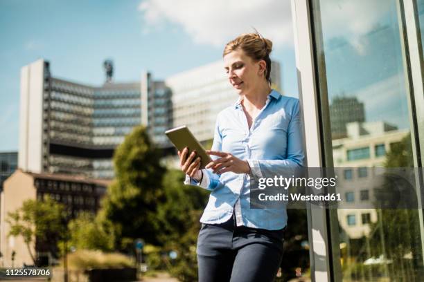 smiling woman leaning against a building using tablet - essen ruhrgebiet stock-fotos und bilder