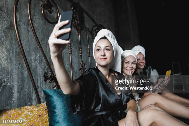 three women with towels around her heads on bed taking a selfie - three people bed stock pictures, royalty-free photos & images