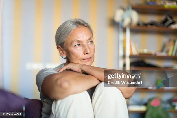 portrait of pensive senior woman sitting on the couch at home - introspectie stockfoto's en -beelden