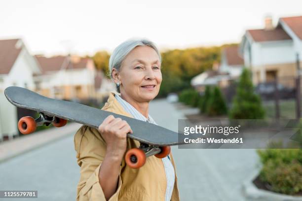 portrait of smiling senior woman with skateboard on her shoulder - young at heart stock-fotos und bilder