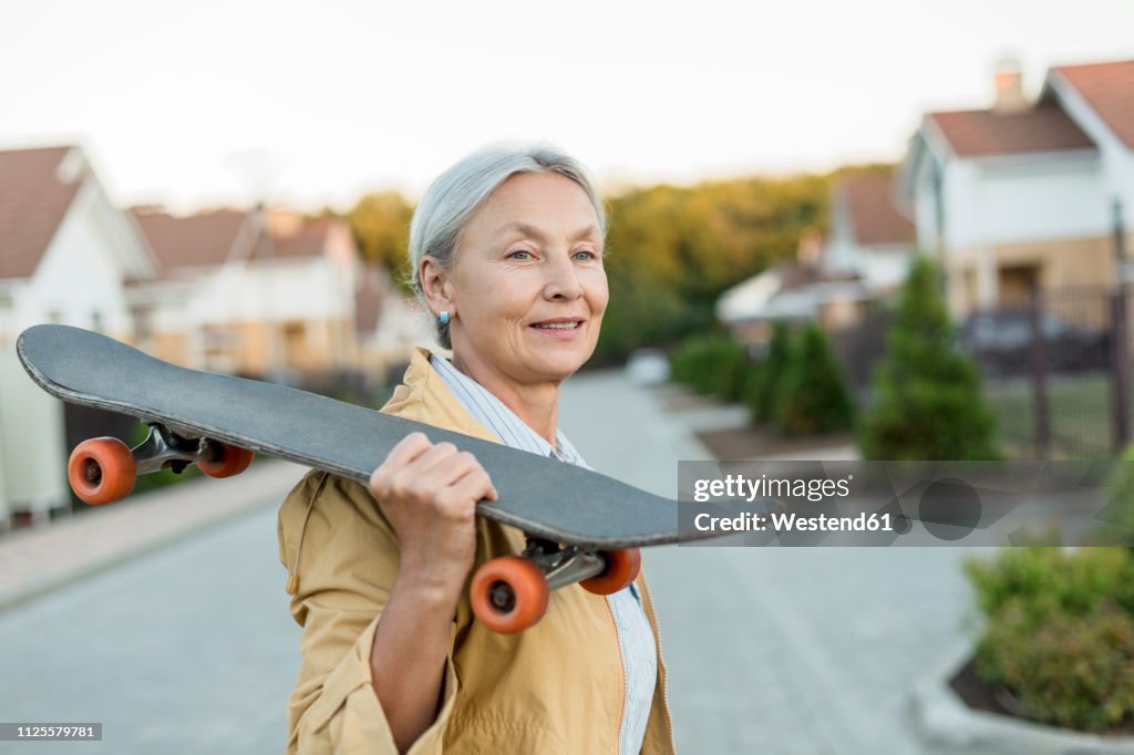 Portrait of smiling senior woman with skateboard on her shoulder