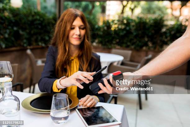 woman paying with smartphone in a restaurant - paid stockfoto's en -beelden