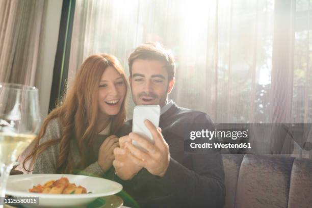 happy couple looking at cell phone in a restaurant - couple in surprise stock pictures, royalty-free photos & images