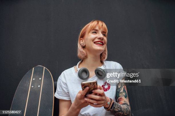 happy young woman with skateboard, headphones and cell phone - geração y imagens e fotografias de stock