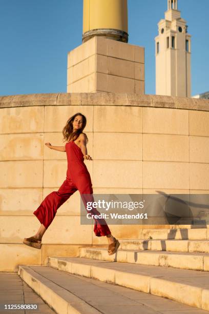 spain, barcelona, montjuic, young woman wearing red jumpsuit jumping on stairs - red jumpsuit stock pictures, royalty-free photos & images