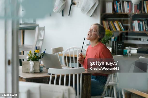 young woman sitting at table in a cafe with laptop and drumsticks - baqueta instrumento musical - fotografias e filmes do acervo