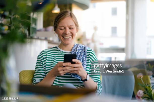 laughing young woman looking on cell phone in a cafe - candid forum stockfoto's en -beelden