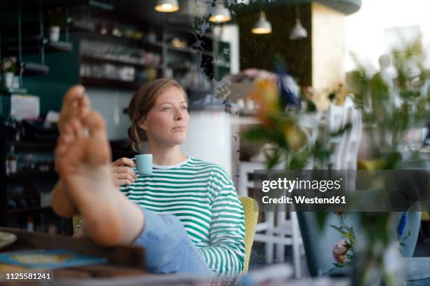 young woman with feet up holding espresso cup in a cafe - espresso trinken stock-fotos und bilder