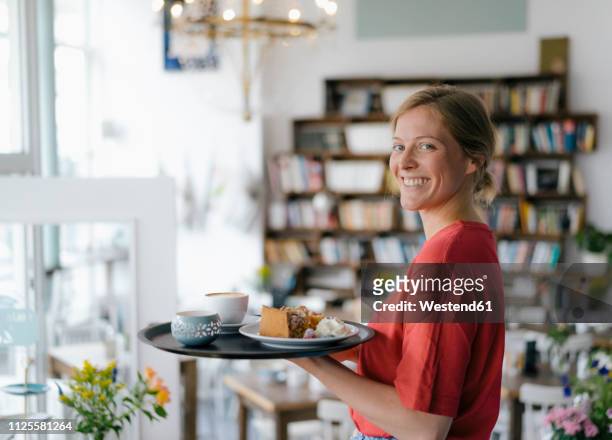 portrait of smiling young woman serving coffee and cake in a cafe - woman holding cake stock-fotos und bilder