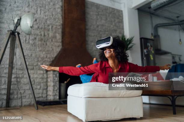 woman lying on seating furniture, wearing vr goggles, pretending to fly - flying goggles imagens e fotografias de stock