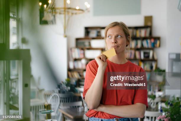 young woman holding card in a cafe thinking - pessimisme stock pictures, royalty-free photos & images