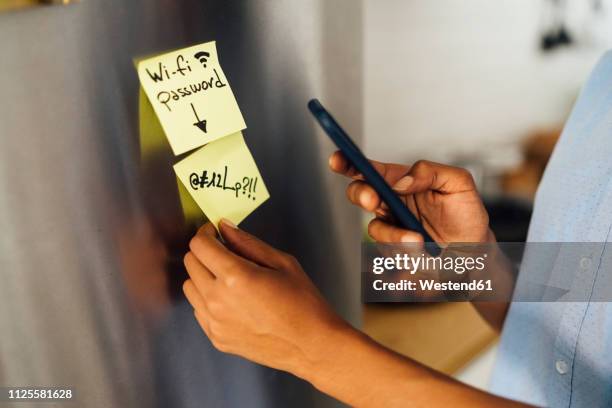 woman in her kitchen in the morning, posting sticky notes on the fridge - passwort stock-fotos und bilder