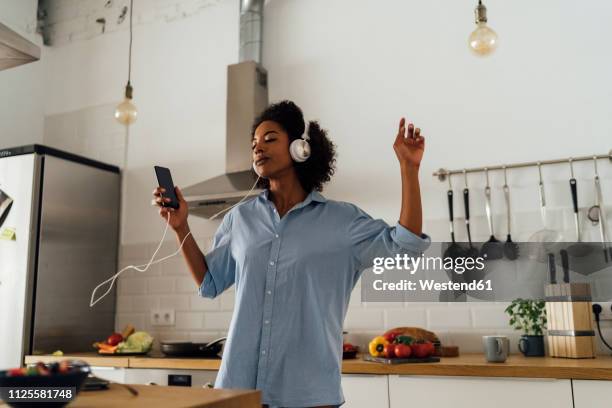 woman dancing and listening music in the morning in her kitchen - frau kopfhörer indoor stock-fotos und bilder