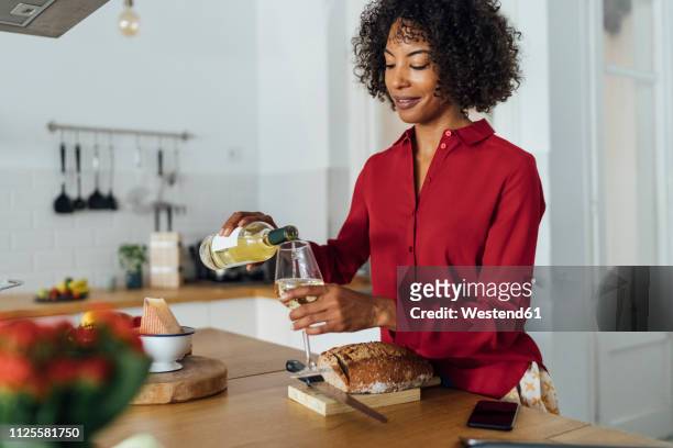 woman standing in kitchen, pouring herself a glass of white wine - drinking alcohol at home photos et images de collection