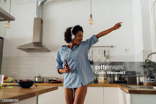 woman dancing and listening music in the morning in her kitchen - stressfrei stock-fotos und bilder