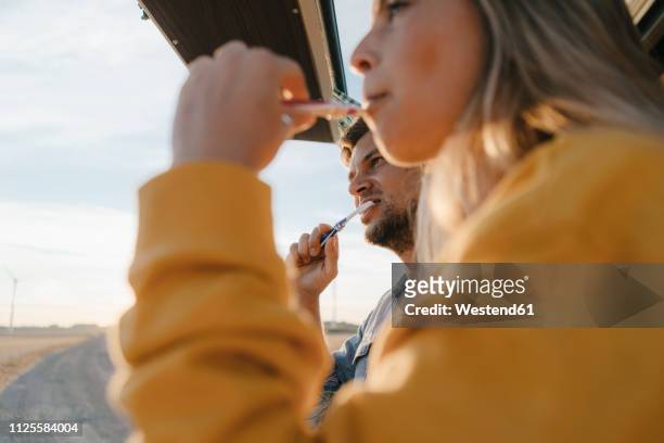 couple brushing teeth in camper van in rural landscape - zähne putzen stock-fotos und bilder