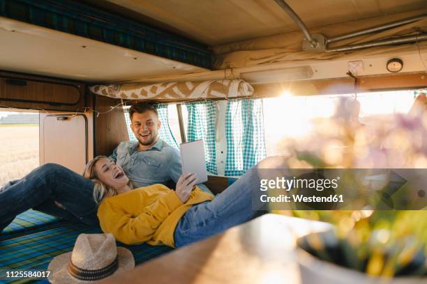 happy young couple looking at tablet inside camper van - camping couple stockfoto's en -beelden