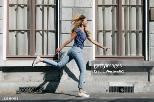 netherlands, maastricht, happy blond young woman running along building in the city - happy people running stockfoto's en -beelden