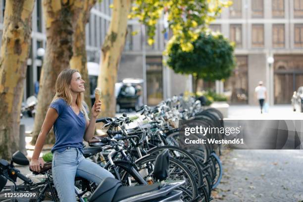 netherlands, maastricht, smiling blond young woman holding ice cream cone in the city at bicycle rack - years of the kingdom of the netherlands in maastricht stockfoto's en -beelden