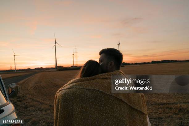 couple wrapped in a blanket at camper van in rural landscape with wind turbines in background - camping couple stock pictures, royalty-free photos & images