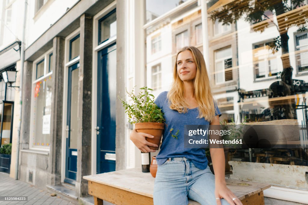 Netherlands, Maastricht, blond young woman holding flowerpot in the city