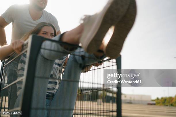 carefree young man pushing girlfriend in a shopping cart - man pushing cart fun play stock pictures, royalty-free photos & images