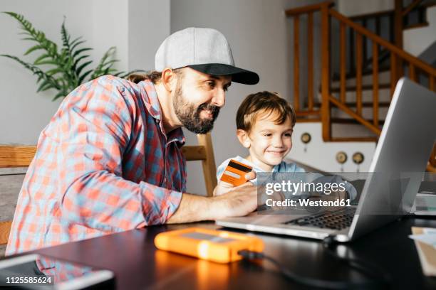 father and son using laptop together, online shopping - shopping credit card stock-fotos und bilder