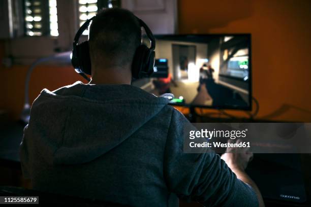 young man sitting at his pc, playing computer games - computerspieler stock-fotos und bilder