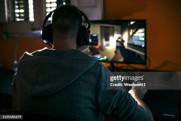 young man sitting at his pc, playing computer games - videojuegos fotografías e imágenes de stock