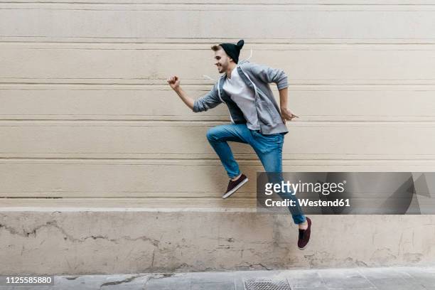 happy young man jumping in front of a wall - youth culture speed stock pictures, royalty-free photos & images