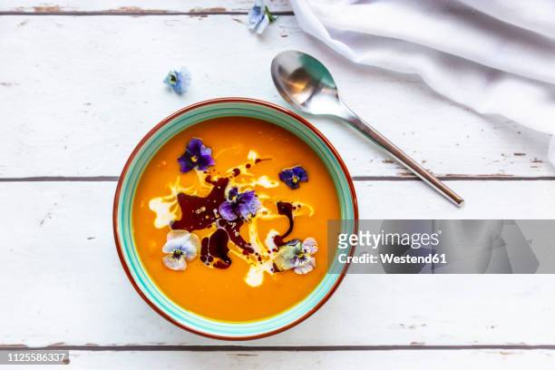 bowl of creamed pumpkin soup garnished with edible flowers - soup bowl stock pictures, royalty-free photos & images