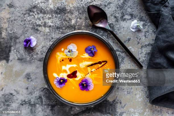 bowl of creamed pumpkin soup garnished with edible flowers - kürbissuppe stock-fotos und bilder