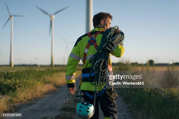 technician walking on field path at a wind farm with climbing equipment - bergbeklimartikelen stockfoto's en -beelden
