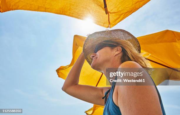 smiling woman wearing straw hat under sunsahde in sunlight - sunshade stock pictures, royalty-free photos & images